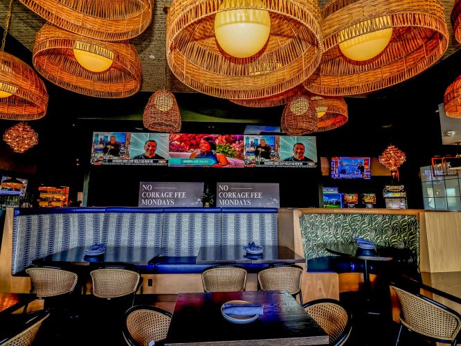 Interior restaurant seating with blue booths, woven light fixtures, and multiple large TVs showing sports news.
