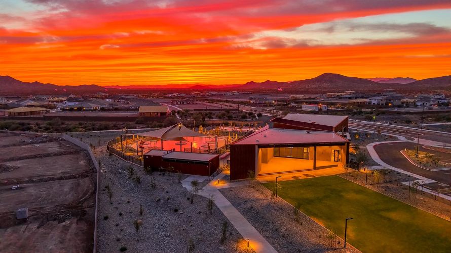 Desert building exterior with a green lawn and pool beneath a glowing red sunset