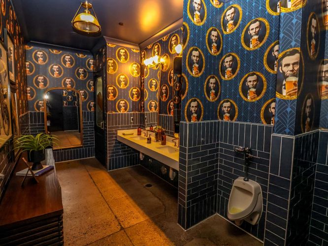 A uniquely decorated restroom with Abraham Lincoln wallpaper and blue subway tile.