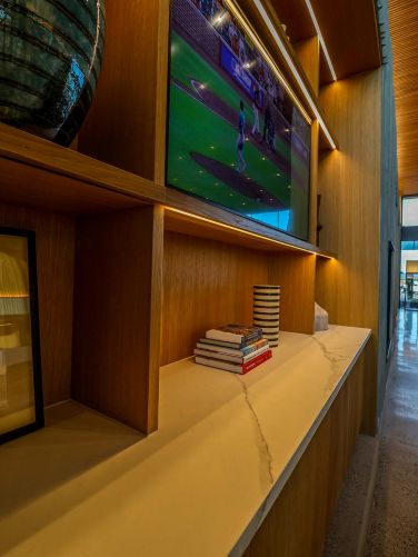 Close-up of wooden built-in shelving with books, a striped vase, and a television showing sports