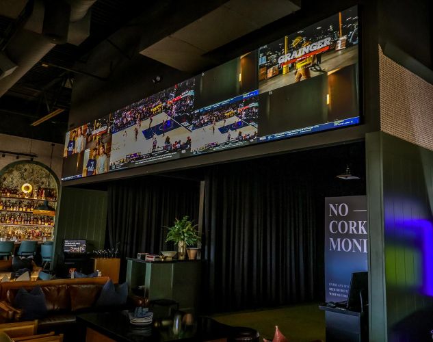 A dark lounge area with a massive projection screen showing basketball and a sign.