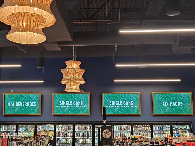 Interior view of a liquor store featuring organized shelves of spirits and blue digital signage for different beverage categories.