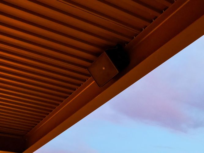 Corrugated metal patio ceiling and mounted speaker against a twilight sky