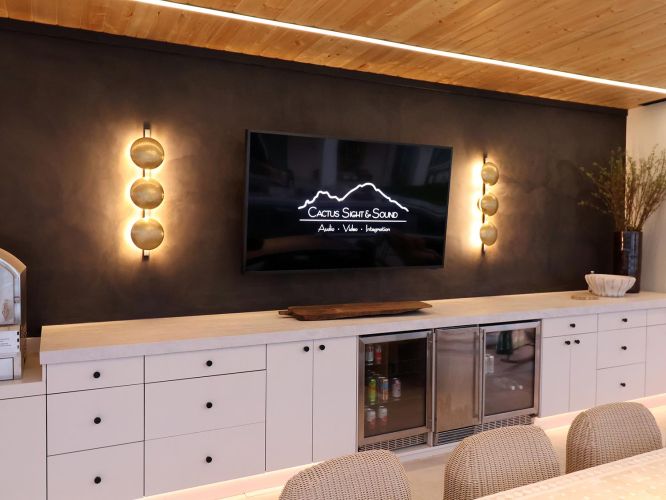 Modern outdoor bar with white drawers and beverage coolers under a television