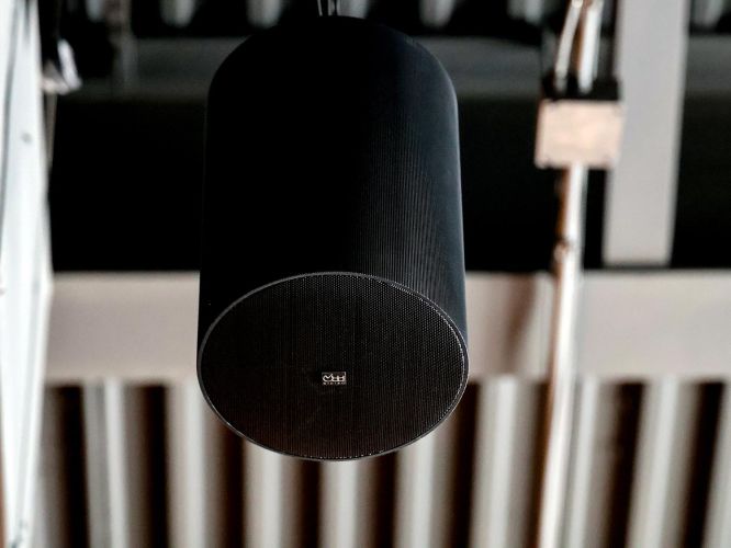 Extreme close-up of a sleek, black cylindrical pendant speaker hanging from the ceiling.