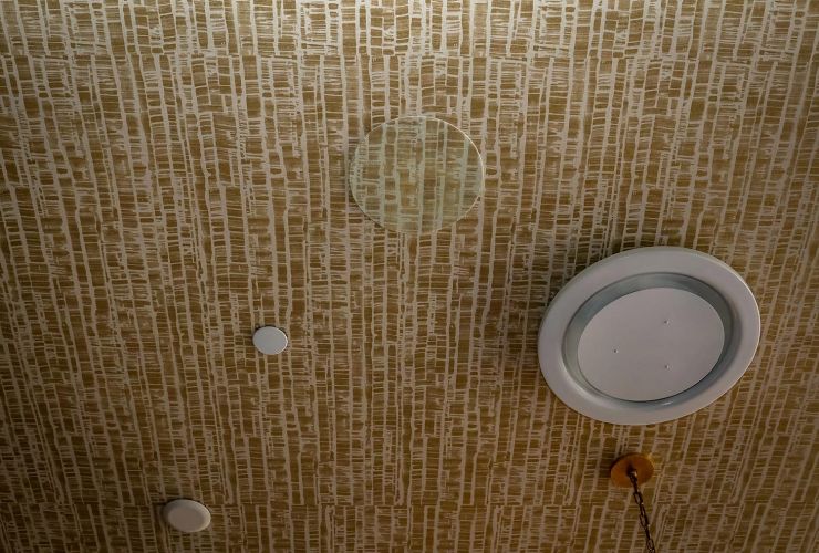 Ceiling detail showing a circular vent, small sensors, and patterned tan wallpaper.