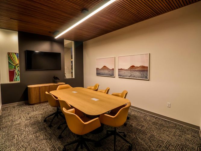 Modern meeting room with a wooden table, yellow office chairs, a TV, and framed artwork