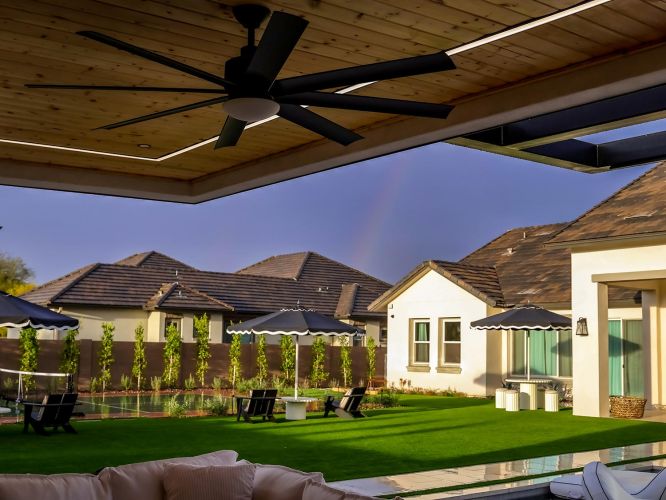 Modern patio view of a green lawn with black umbrellas and a wooden ceiling fan