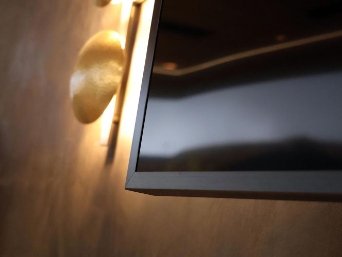 Detail of a sleek black television frame next to a glowing gold wall light