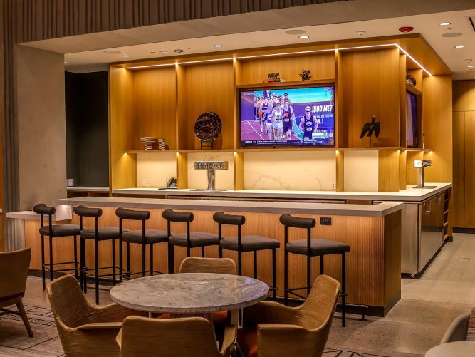 Modern interior bar with leather barstools, a marble counter, and beer taps under a TV