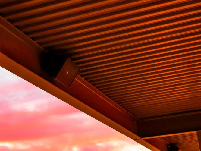 Close-up of a corrugated metal patio ceiling and speaker against a pink sunset sky