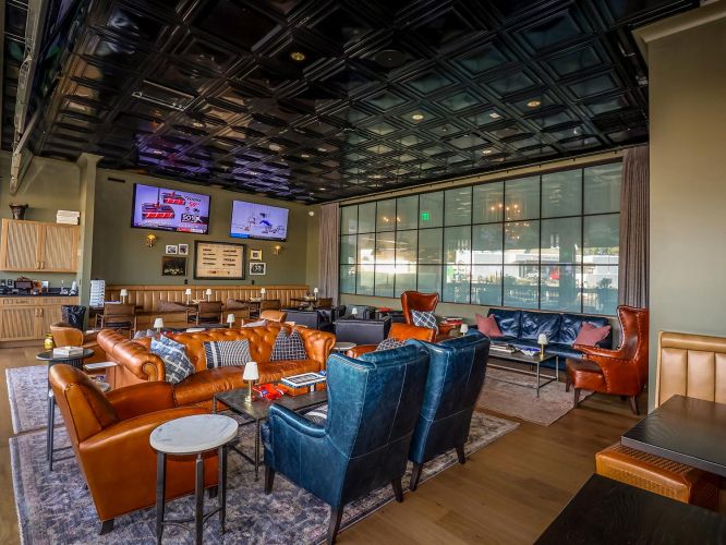 A cozy cigar lounge with leather sofas, blue velvet armchairs, and a black coffered ceiling.