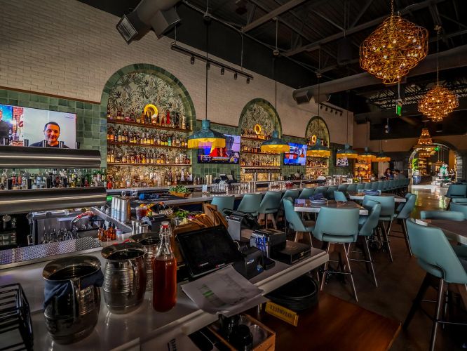 Behind-the-bar perspective showing beer taps, cocktail prep areas, and the teal-stooled seating area.