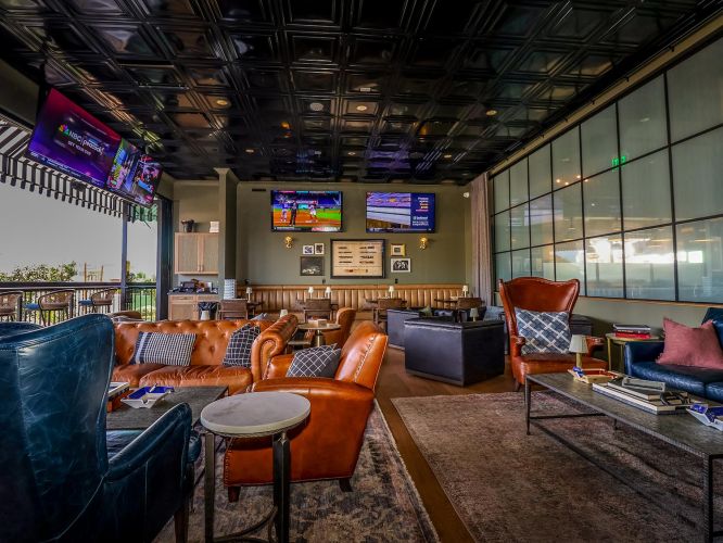 Interior of a lounge area featuring multiple TVs, comfortable leather seating, and a large glass partition.