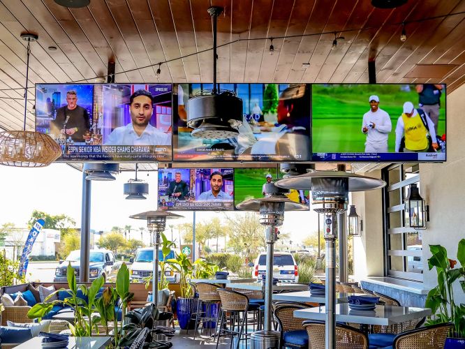 Patio area featuring outdoor heaters, plants, and a large overhead TV array.