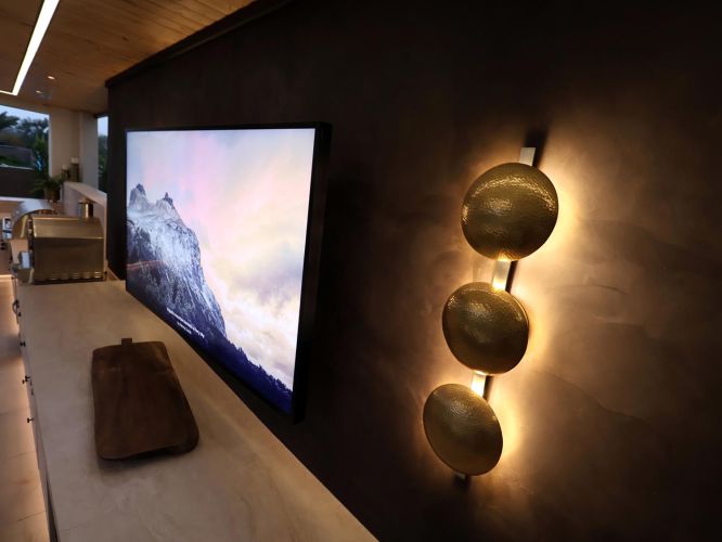Side view of a flat screen television and triple gold sconce on a dark patio wall
