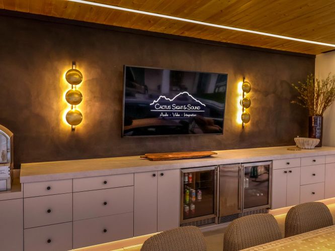 Outdoor kitchen area with white cabinetry and a television flanked by gold sconces