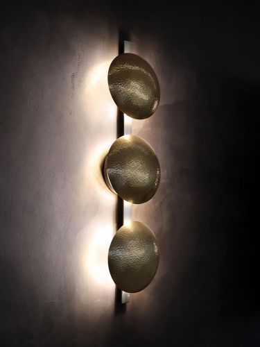 Vertical trio of hammered metal sconces casting warm light on a dark wall