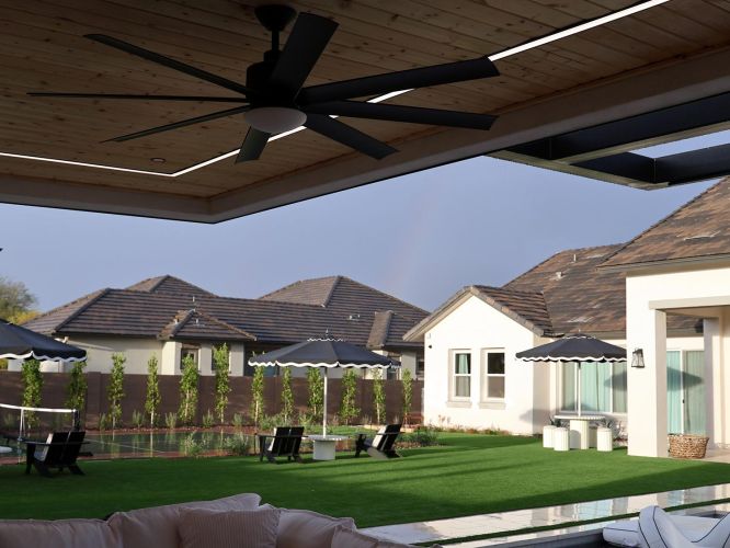 Black ceiling fan on a wood ceiling overlooking a manicured lawn and residential homes