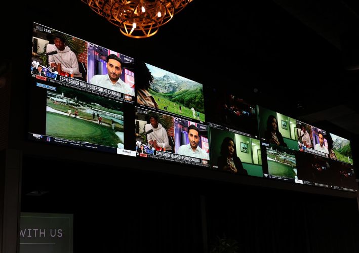 A massive multi-screen TV display showing various sports news and golf clips simultaneously.