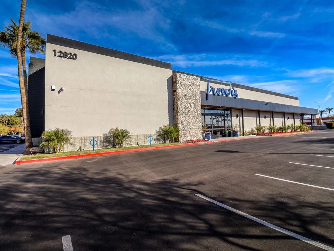 Exterior daytime shot of Trevor's building showing a modern facade with stone accents and a large parking area.