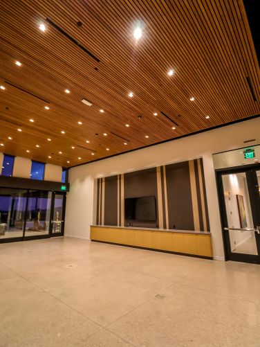 Spacious empty event room featuring a wood-slat ceiling and glass exit doors
