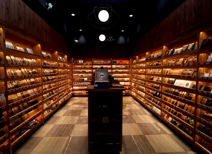 Interior of a walk-in cigar humidor with floor-to-ceiling wooden shelves filled with cigar boxes.