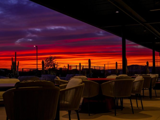 Covered outdoor patio with lounge seating looking out at a vibrant red and purple sunset