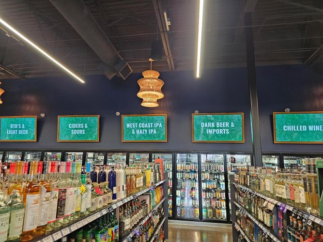 Symmetrical shot of liquor aisles under bright linear LED lighting with category signs