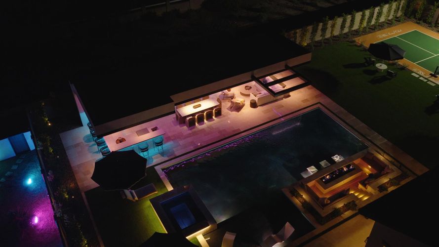 Aerial view of a modern backyard with pool and sports court at night