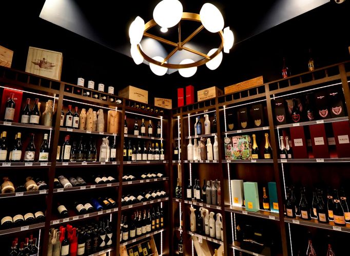 A luxury wine display area with a circular modern chandelier and dark wood shelving.