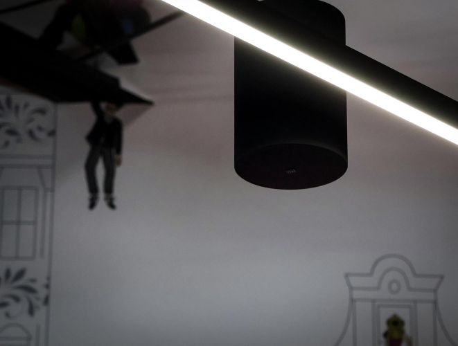 Artistic shot of a black pendant speaker and a linear light against a white wall with line-art drawings.