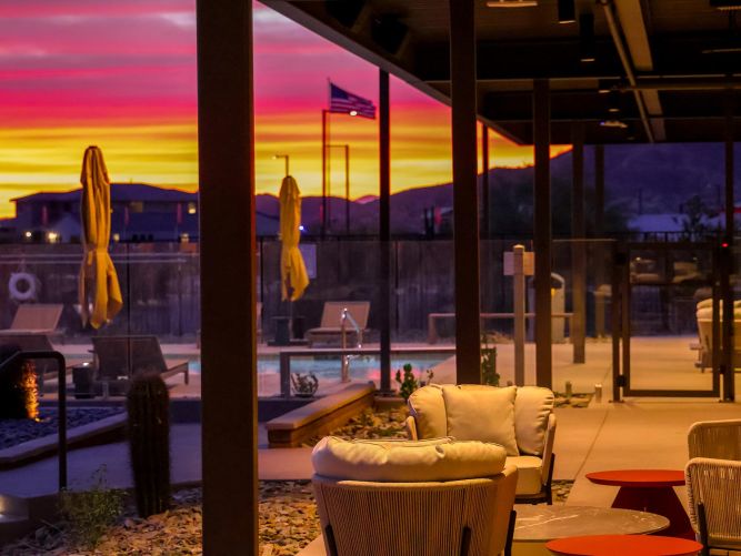 Outdoor patio seating area with a view of a pool and flag pole during a colorful sunset