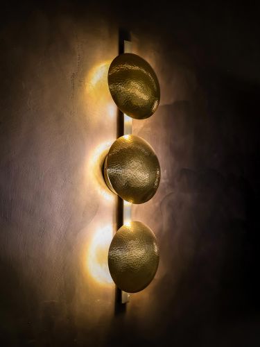Three glowing gold disc wall sconces mounted on a dark textured wall